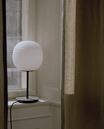 Terra Bordslampa från New Works i fönster med bruna gardiner