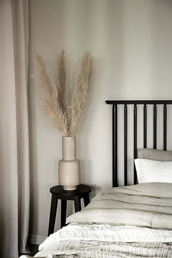 Austin Barpall i svartlackad ek som sängbord intill säng med en vas med pampas